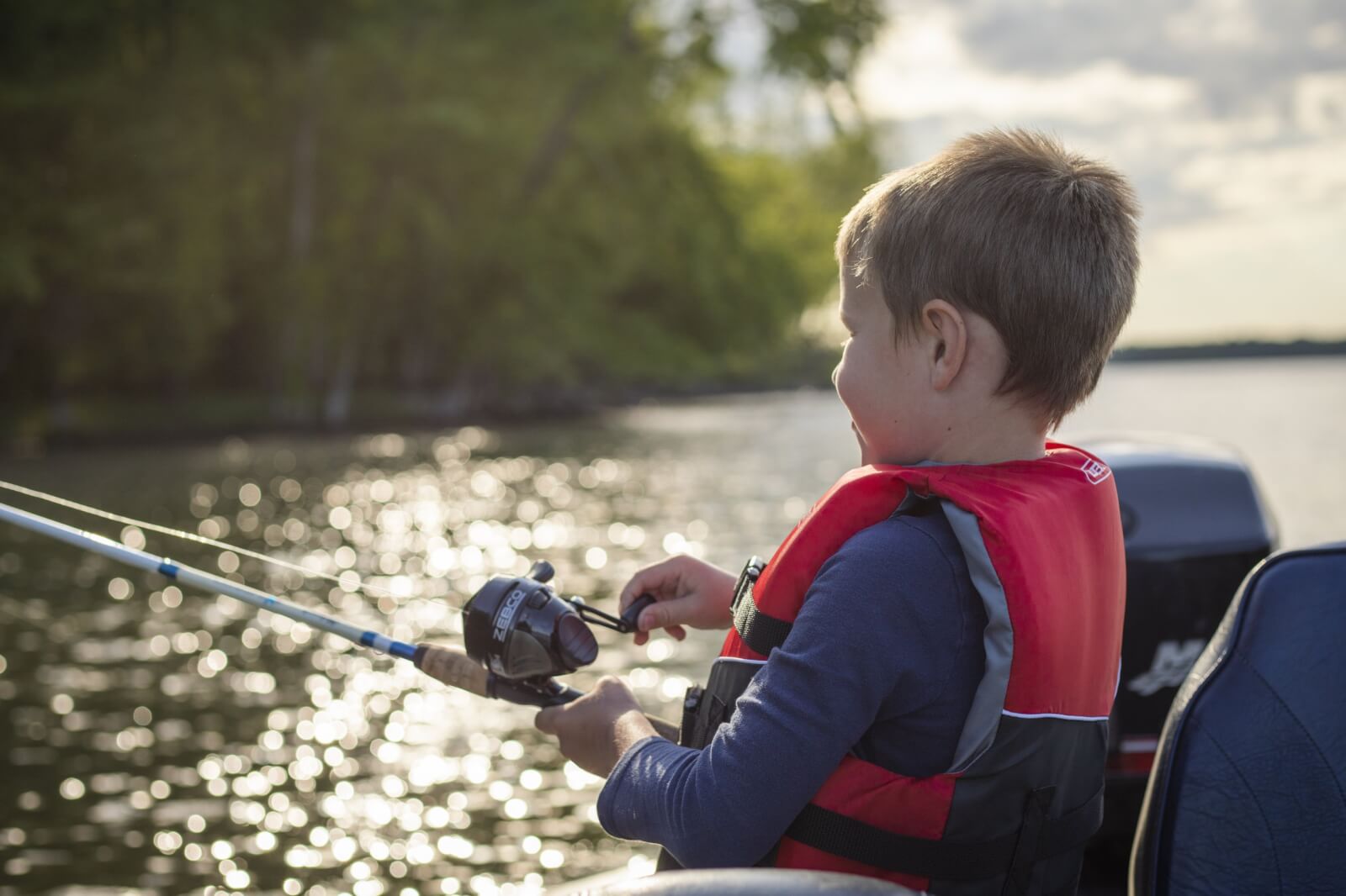 Young boy in a red vest  holding a fishing rod and Fashioning on a lake