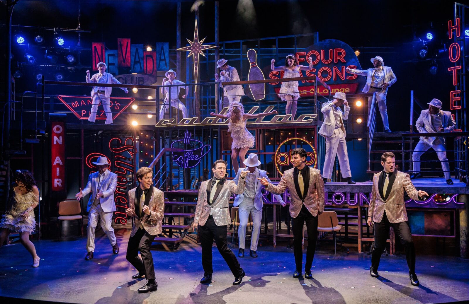 2025 Live Theatre Is Magical: Why I Believe in the Power of the Stage The Rev Theatre production of the Jersey Boys, showing 5 men on stage in gold blazers singing with many background dancers in white.