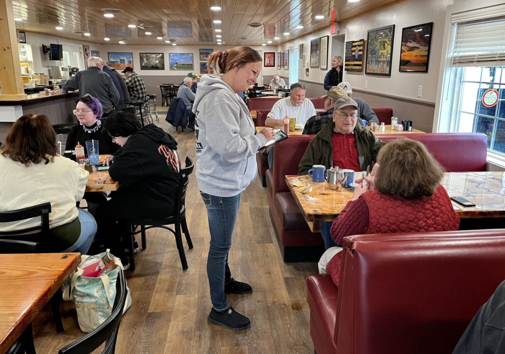 Waitress waiting on a couple sitting in a booth and a variety of diners sitting at tables and booths enjoying their food