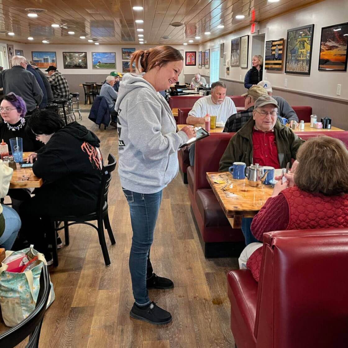 Waitress waiting on a couple sitting in a booth and a variety of diners sitting at tables and booths enjoying their food