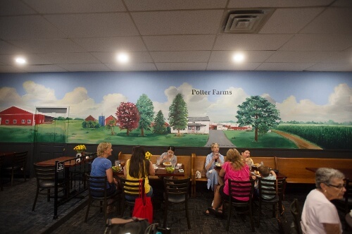 Interior of a restaurant with a large mural of the country side on the back wall