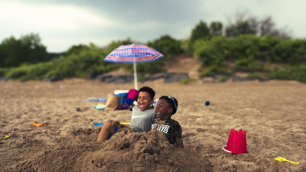 two young boys playin in the sand with a beach umbrella in the background