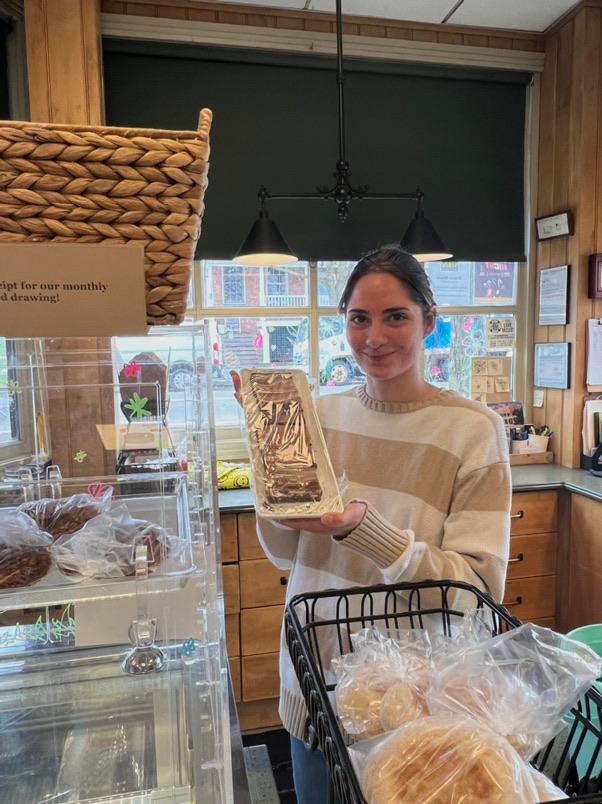 young dark hair woman in a small store holding a tray of sliced bakes bread