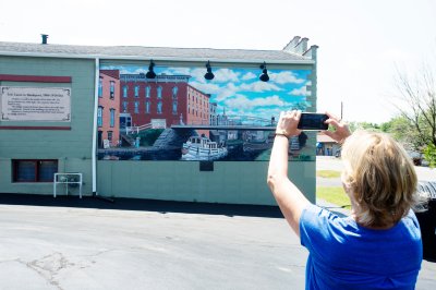 Person taking a picture of murals depicting life on the Erie Canal