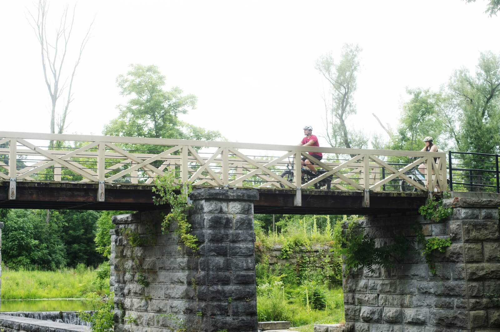 Two adults on bikes riding over an aqueduct on an Erie Canal Trail