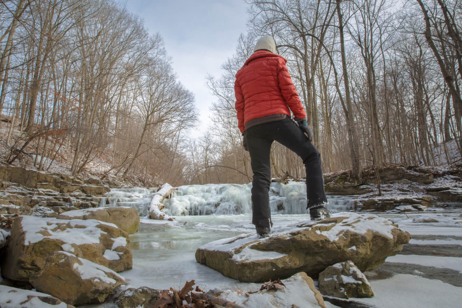 A woman in a red coat hiking and standing next to a frozen waterfall