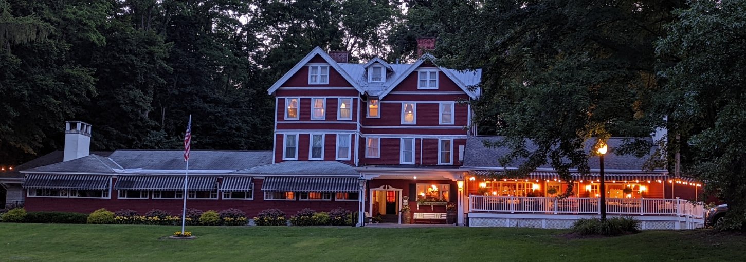The red and white façade of a historic inn has a porch lied with lights.