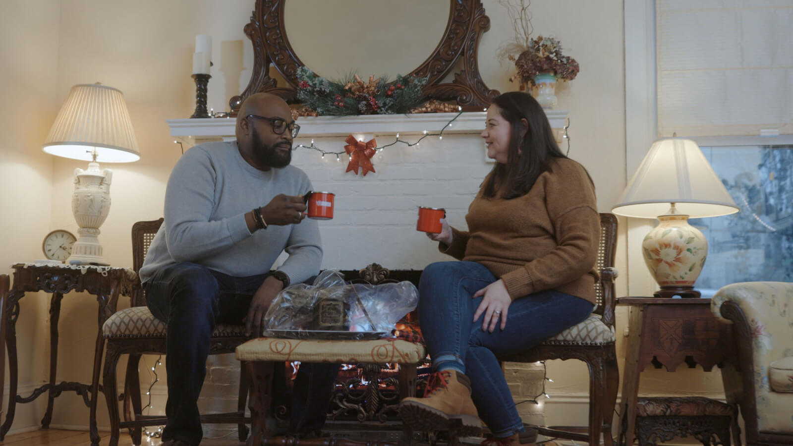 A couple enjoys a hot beverage in front of a glowing fire. A cozy living room in a home rental.