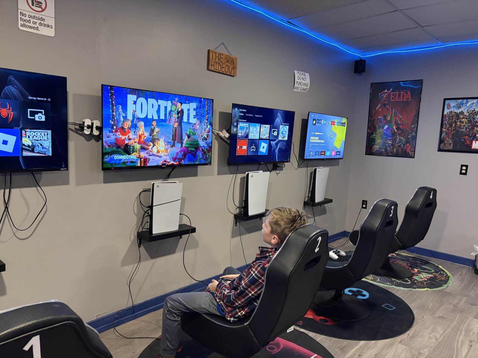 young boy sitting in a gaming chair infront of a row of tv's with video games playing