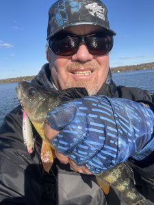 man with the lake in the background, holding a fish with a lure hanging out of the fishes mouth