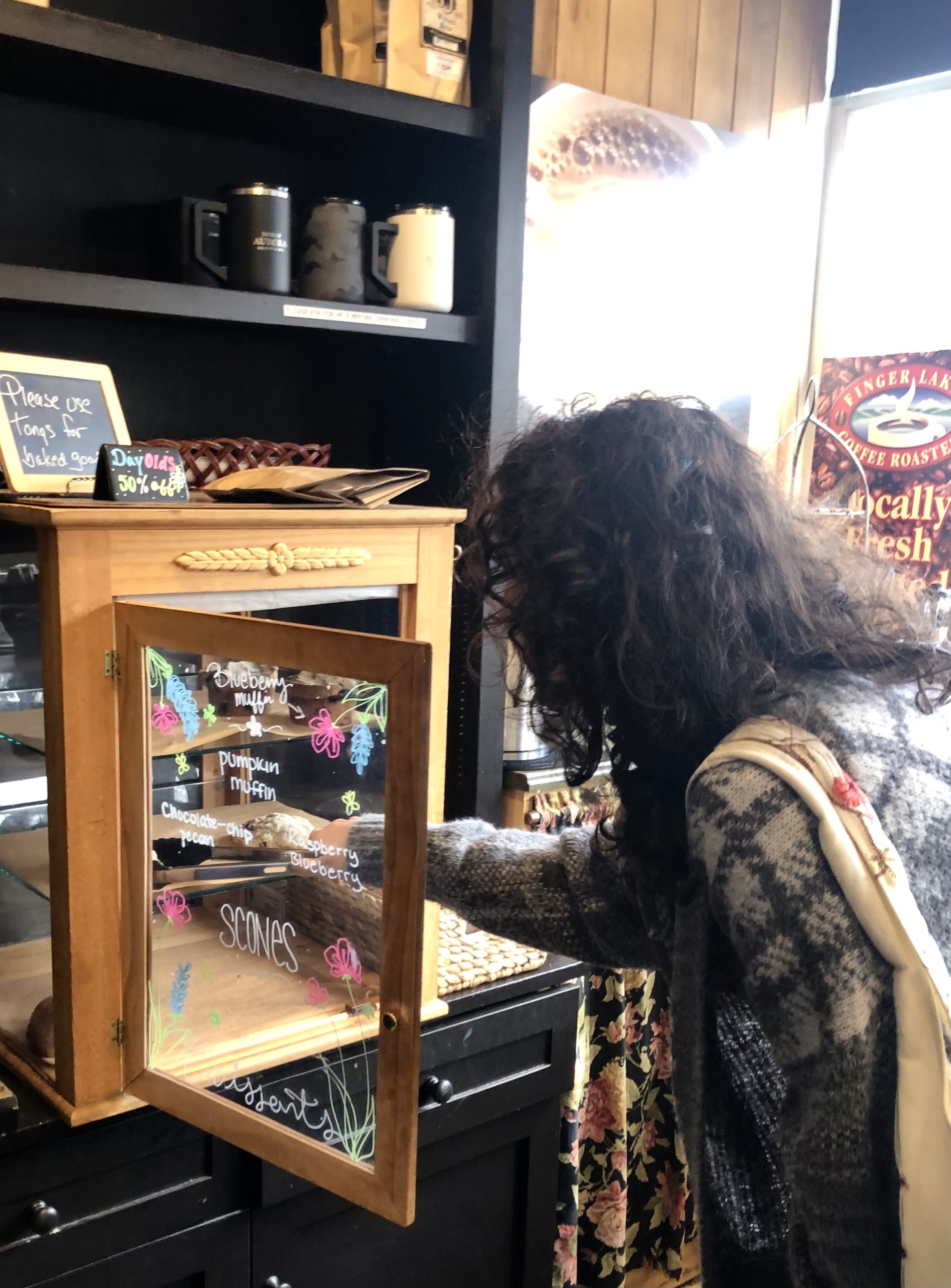 woman with dark hair helping herself to a sweet treat from a glass case