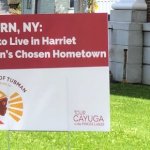 A red and white sign stands in the yard of a house reading: Auburn, NY: Proud to Live in Harriet Tubman's Chosen Hometown.