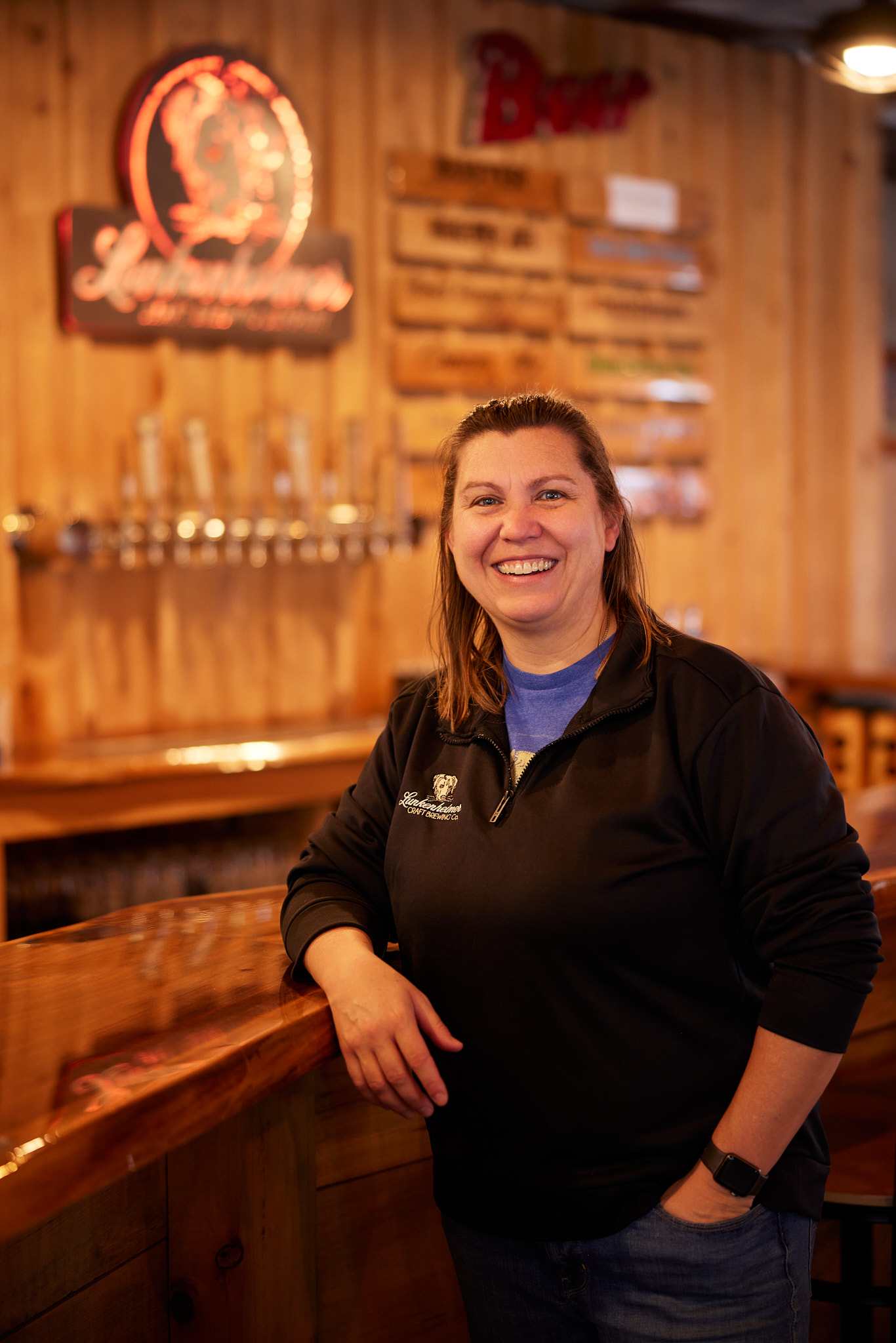 Kristen Lunkenheimer, owner of Lunkenheimer sitting in bar area with Lunkenheimer sign in the background