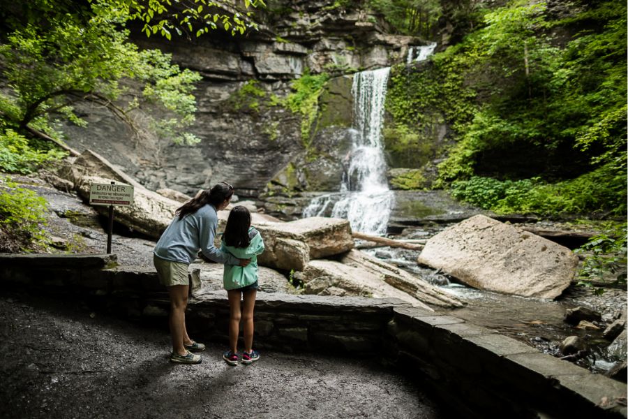 A mother and young daughter looking at a waterfall in the fall at Fillmore Glen State Park