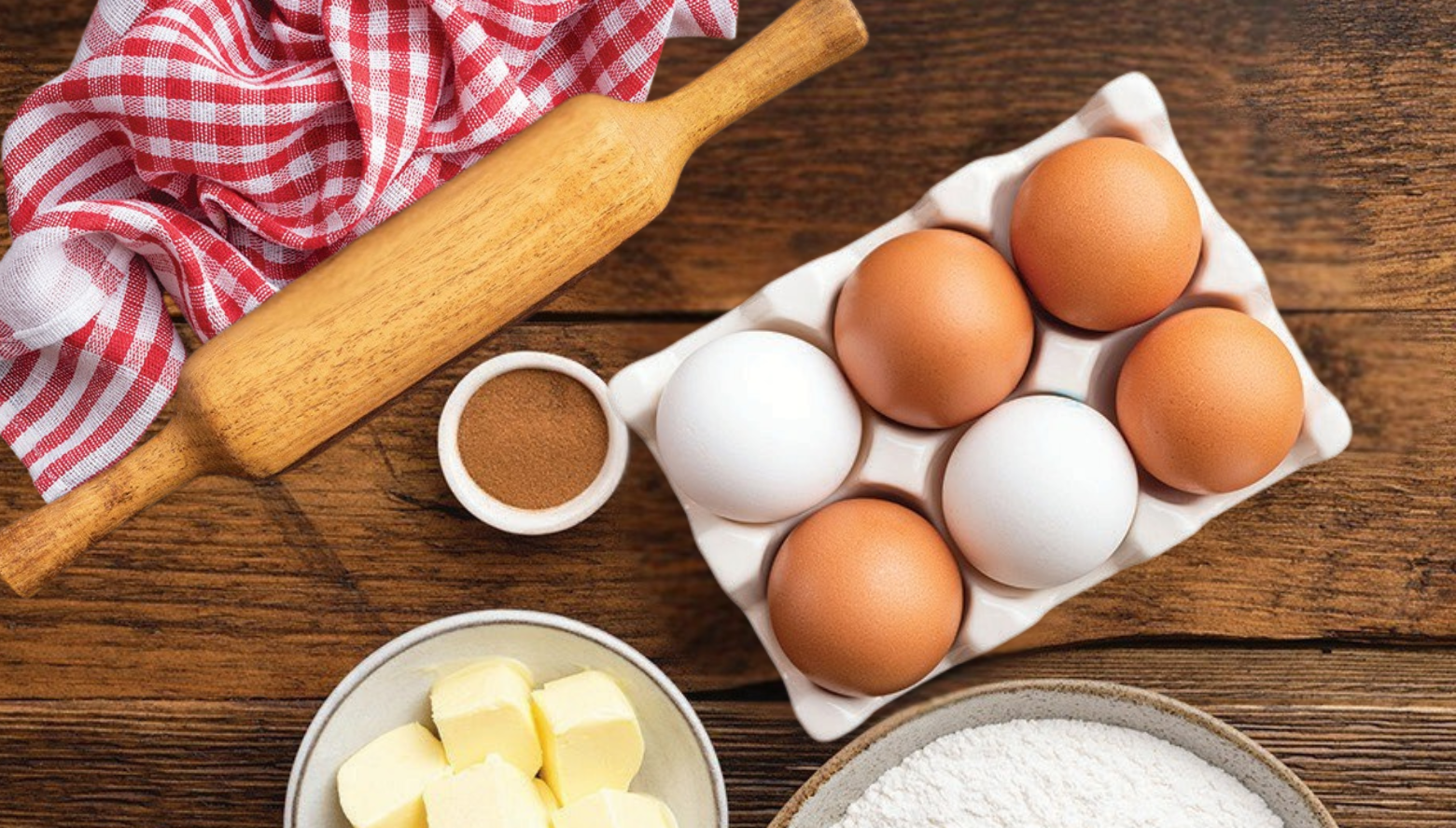 Home Baking Supplies on wooden table. Supplies include rolling pin, eggs and a bowl of butter and flour
