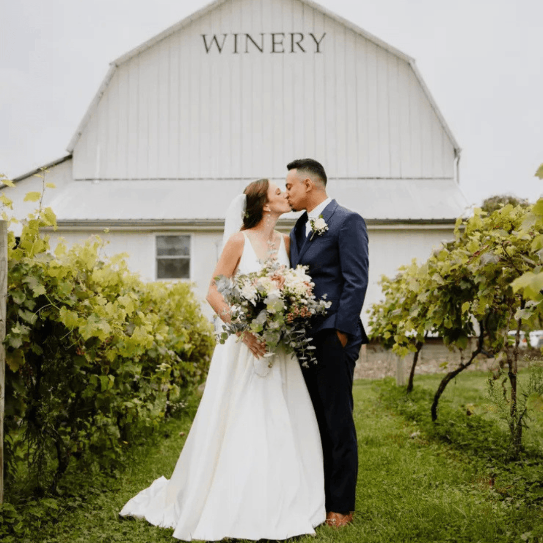 bride and groom standing in a vineyard in futon of a large white barn
