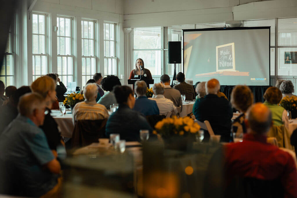 A conference room full of  people listening to a speaker review the agenda