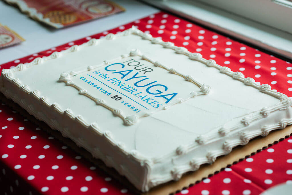 Celebrating 30 Years of Tourism Excellence in Cayuga County: Happy Birthday Tour Cayuga White sheet cake on a red and white polka dot table cloth. Cake has Happy 30th Anniversary Tour Cayuga written on it.