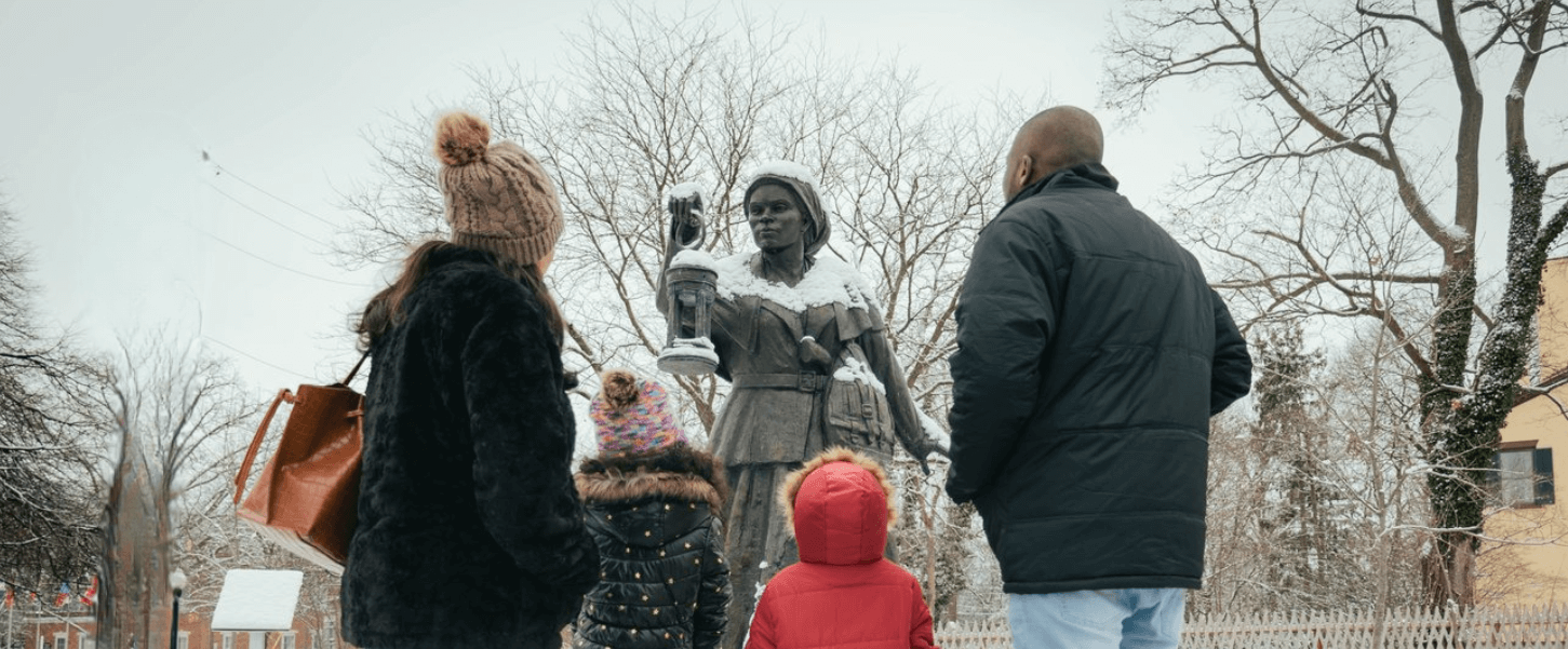 Family in standing in front of the Harriet Tubman Bronze Statue in the courtyard of the Equal Rights Heritage Center in the winter with snow in the ground