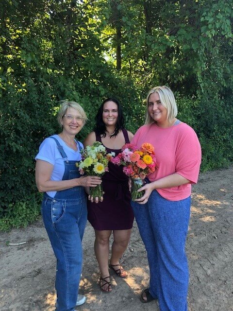 Three women standing showing off freshly picked wild flowers