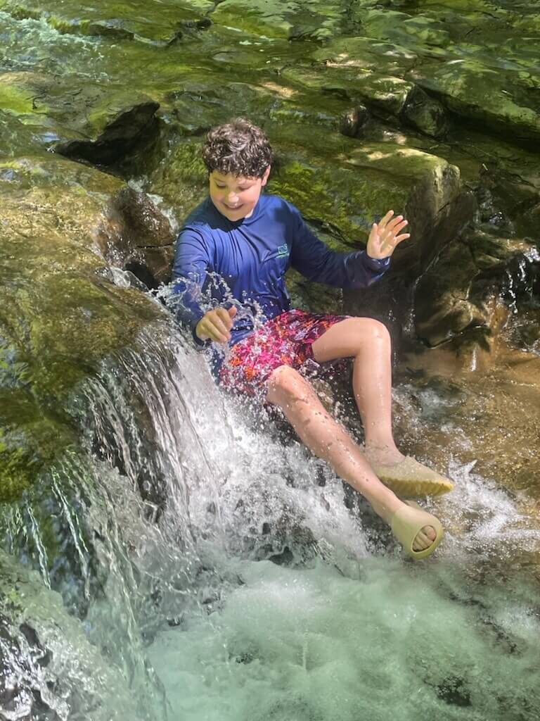 Family Friendly Outdoor Adventures in Cayuga County boy sitting in a small waterfall enjoying an outdoor adventure in the Summer