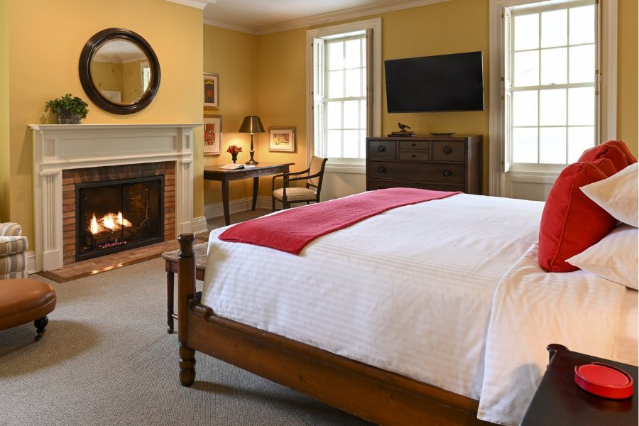 A guest room is decorated in yellow and red and has a fire in the fireplace.